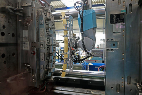 Aufgeschmolzenes Kunststoffgranulat wird zu Bauteilen spritzgegossen, die per Roboterarm entnommen werden