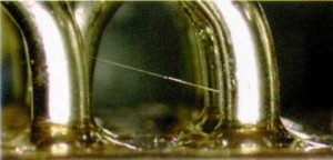 Abb. 1: Der oben abgebildete „Whisker“ aus Zinn wächst zwischen rein verzinnten Hakenanschlüssen eines elektromagnetischen Relais ähnlich MIL-R-6106 (LDC 8913) 