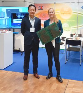 Milena Fritz, CEO SAT Electronic, lobte die Stimmung auf der LOPEC. An ihrer Seite Takayuki Hidehira, CEO MicroCraft. Milena Fritz zeigt eine Demo-Leiterplatte mit Solder Resist-Druck in verschiedenen Dicken, matt und glänzend, sowie mit Legend-Aufschrift